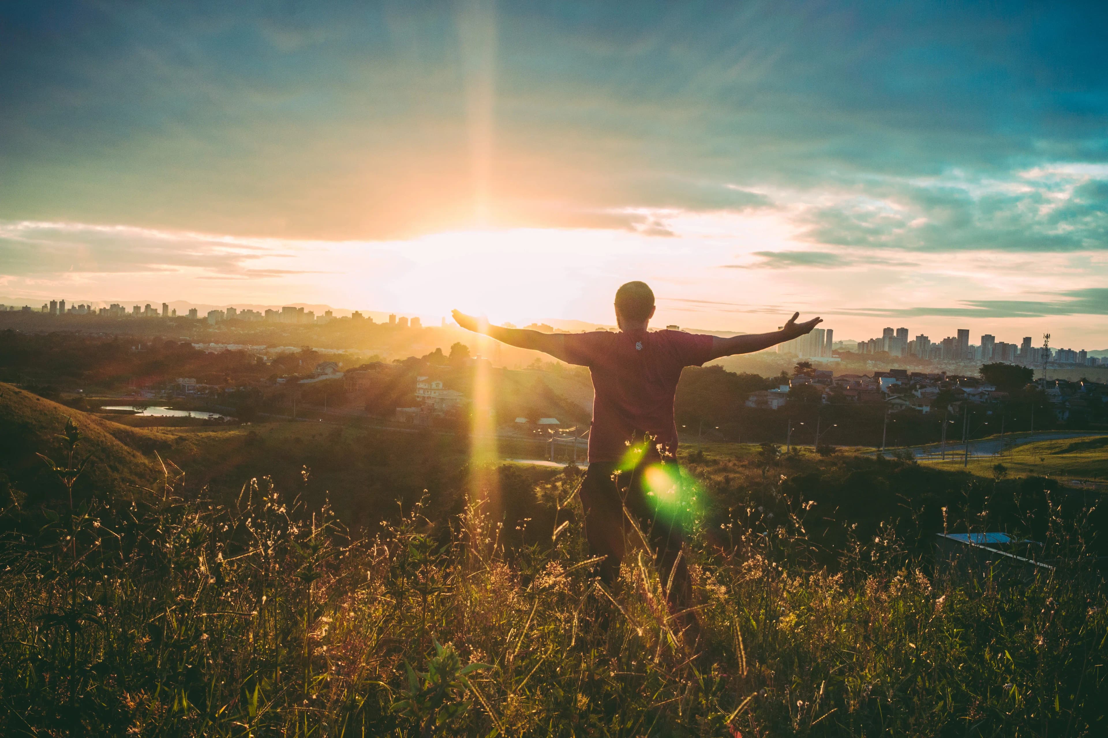 A person embracing freedom, arms outstretched at sunrise